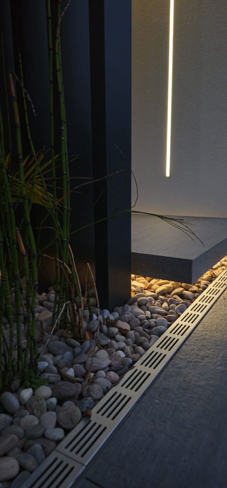 Modern outdoor light fixture on a gravel surface with plants around