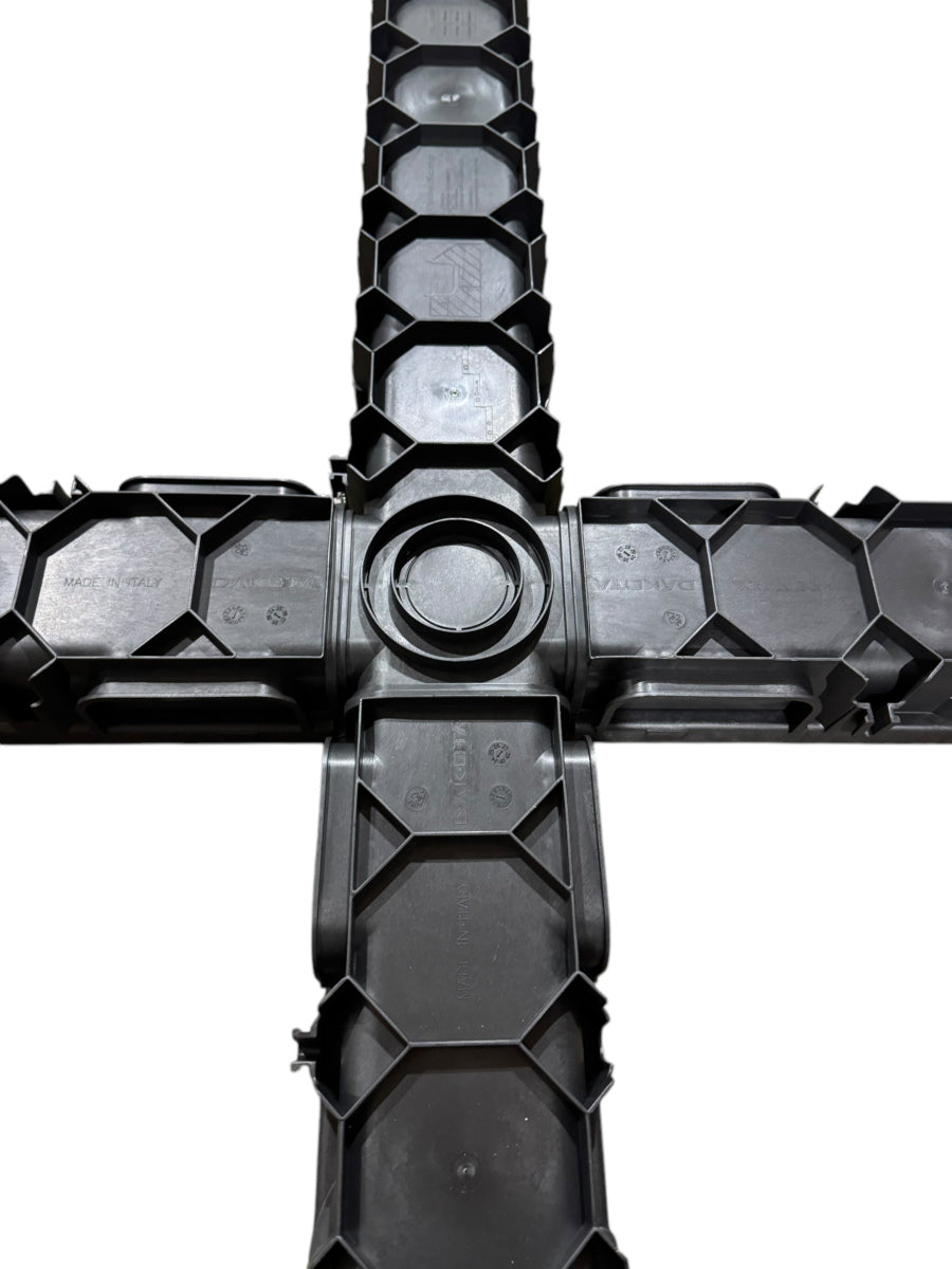 An overhead view of the underside of four channel drain sections connected to form a cross shape, showing a central connector and honeycomb-like structure.