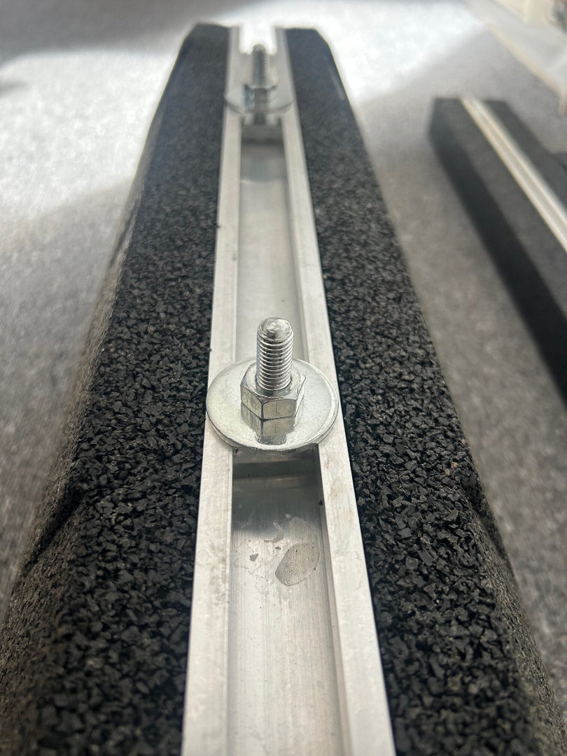 A close-up, downward-angled view of a metal bolt, large washer, and nut secured within the aluminum mounting channel of the black rubber support block.