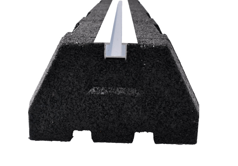 A close-up side view of a textured black rubber mounting block showing its trapezoidal shape, grooved bottom, and the central inset aluminum rail.