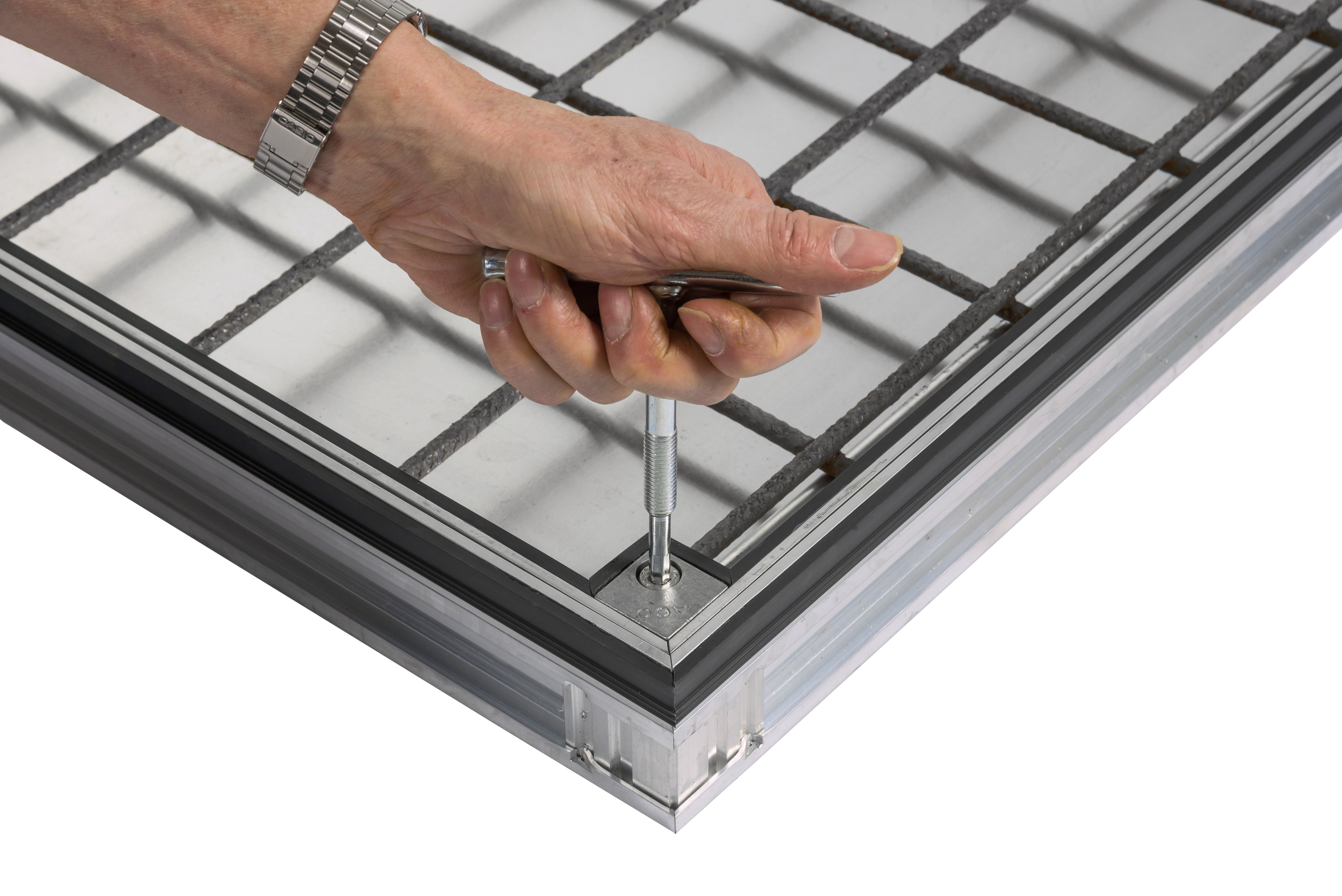 A close-up of a hand using a lifting key to operate the corner locking mechanism on the ACO UniFace AL Shallow vinyl cover.