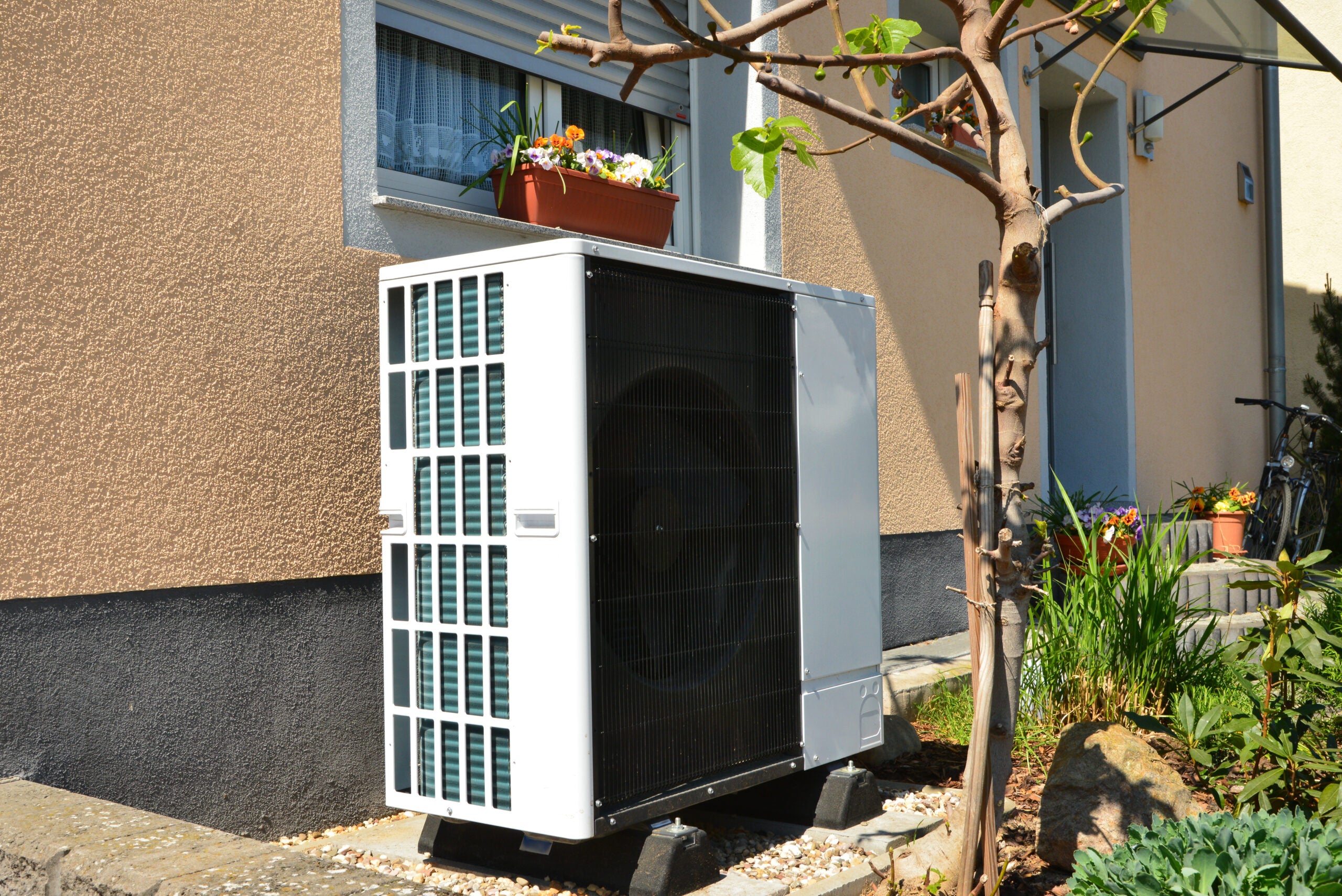 A large, modern white and black outdoor heat pump or air conditioning unit resting on dark support blocks, situated next to a house
